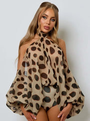A woman modeling a beige halter top with a bold brown and black leopard print pattern, featuring voluminous balloon sleeves and a high neck, set against a plain light gray background.