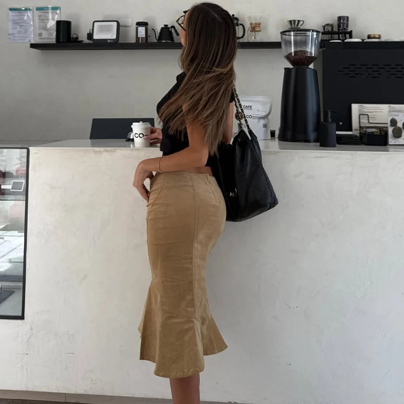 Woman in a beige skirt standing at a counter in a coffee shop.