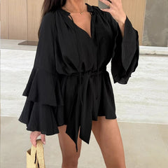 Woman wearing a black dress with ruffled layers in an indoor setting.
