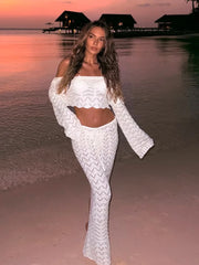 Woman in a white crochet outfit standing on a beach at sunset.