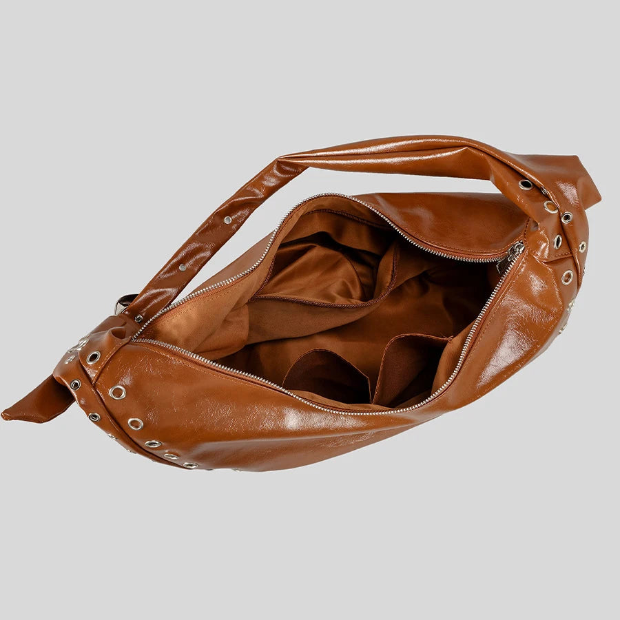 Brown leather handbag with grommet details on a light gray background