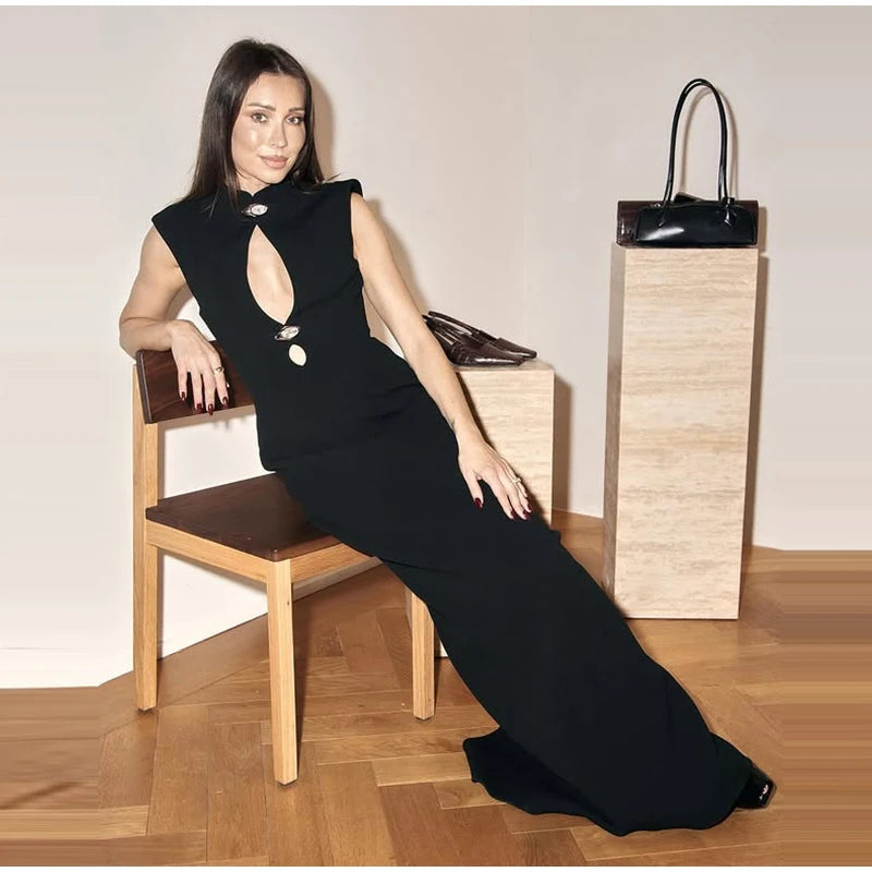 Woman in a black dress sitting on a wooden chair with a black handbag beside her.