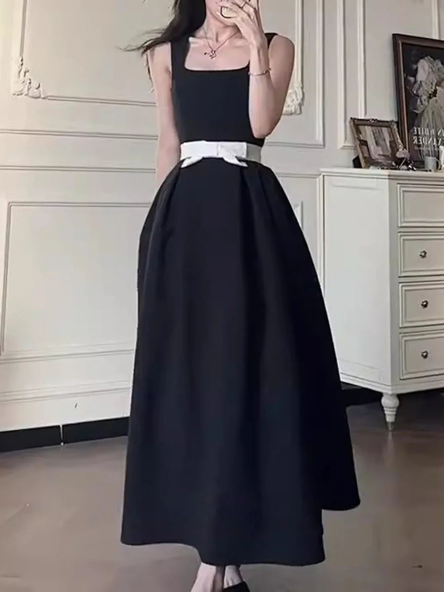 Person wearing a black dress with a white belt in a room.