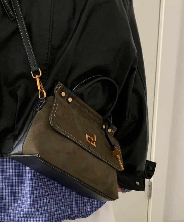 Person wearing a dark green handbag with gold accents, standing indoors.