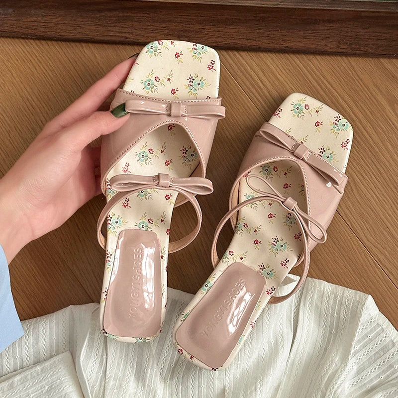 Pair of pink floral sandals with a hand holding one shoe on a wooden surface.