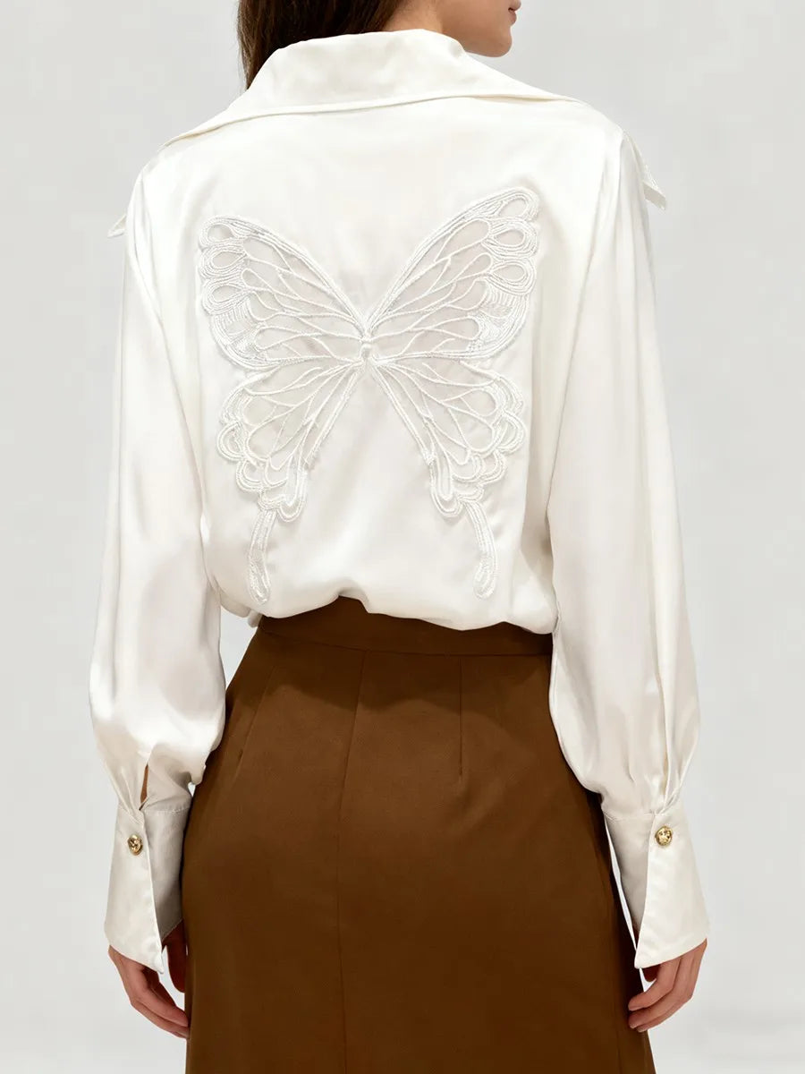 White blouse with butterfly embroidery on a plain background