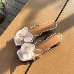 Silver high-heeled shoes with white floral decorations on a wooden surface