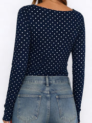 Navy blue long-sleeve top with white polka dots worn by a person, on a plain background