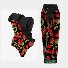 One-shoulder ruched swimsuit with black ruffle detail and cherry print, paired with a wrap skirt cover-up.