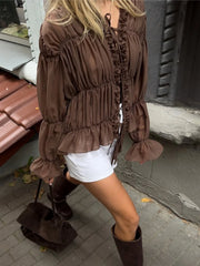 Woman wearing a brown ruffled blouse with white shorts and brown boots on a sidewalk.