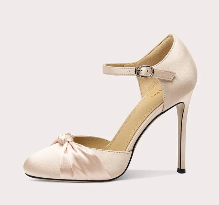 Beige high-heeled shoe with a bow detail on a light gray background