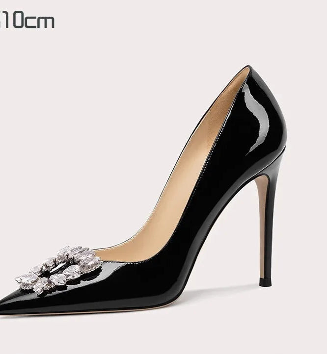 Black high-heeled shoe with a decorative brooch on a light gray background