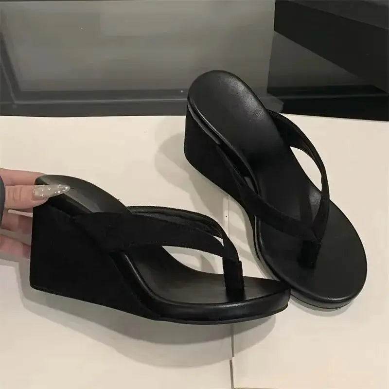 Black wedge sandals on a white surface with a neutral background