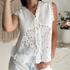 White sleeveless top with lace details worn by a person, with a blurred background.