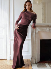 Woman in a burgundy off-shoulder dress standing in a room with white walls and a fireplace.
