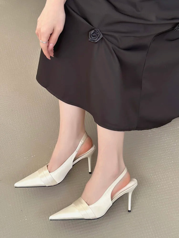 White heeled shoes worn with a black skirt on a neutral background