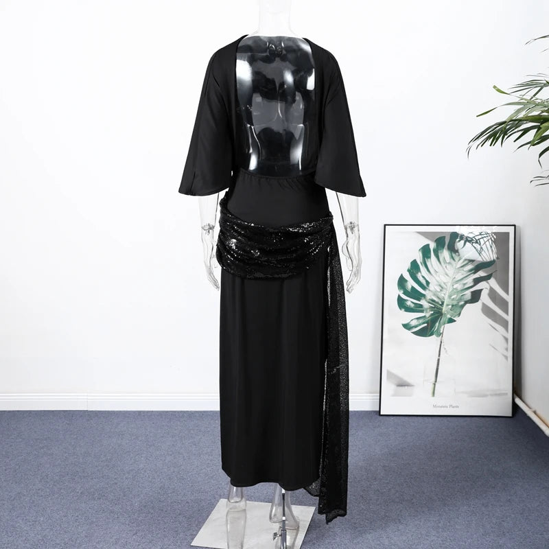 Mannequin wearing a black outfit with a sequined belt in a room with a plant and framed picture.