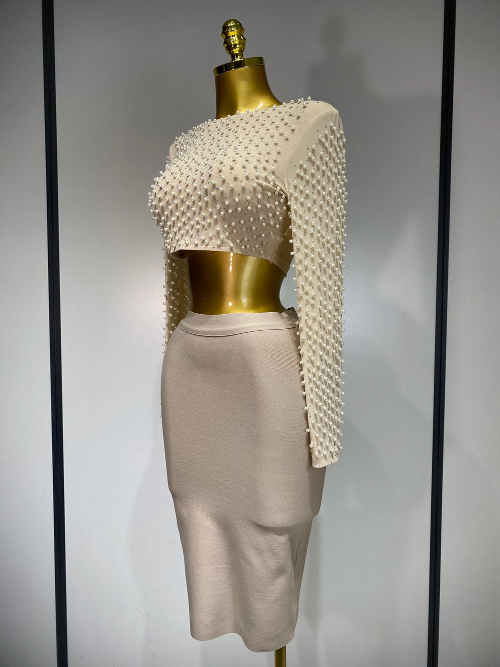 Mannequin wearing a white beaded top and beige skirt against a gray background