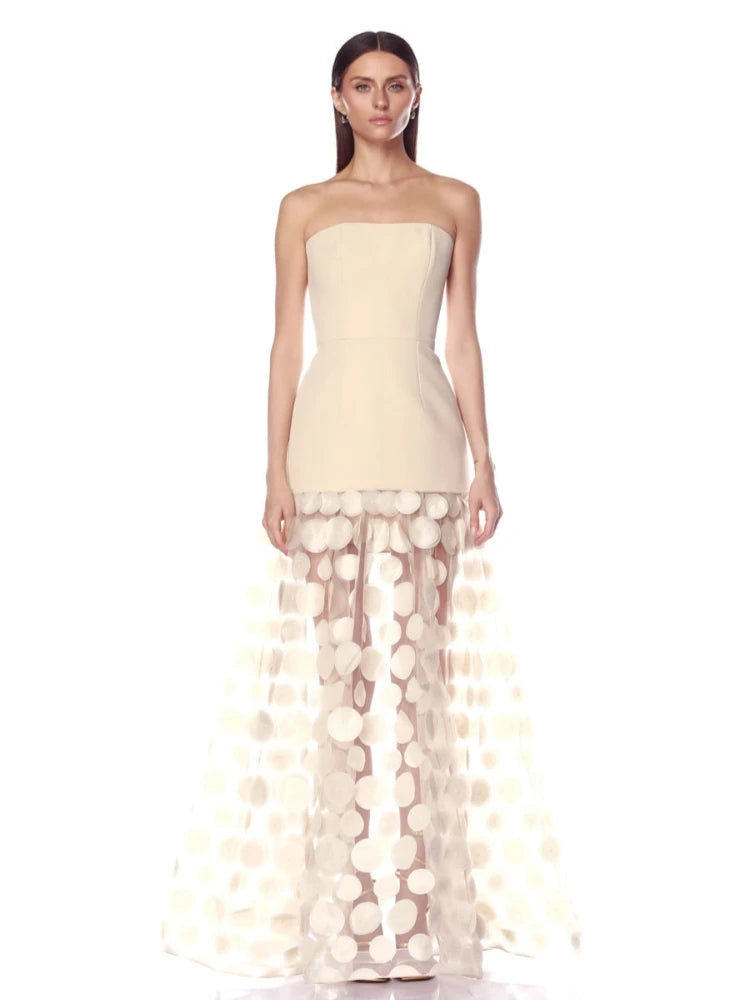 Woman wearing a strapless dress with a sheer, circular patterned overlay on a white background
