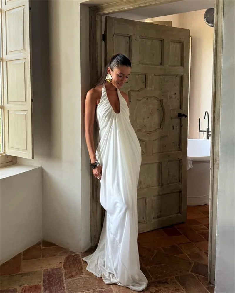 Woman in a white dress standing in a room with a wooden door and tiled floor.