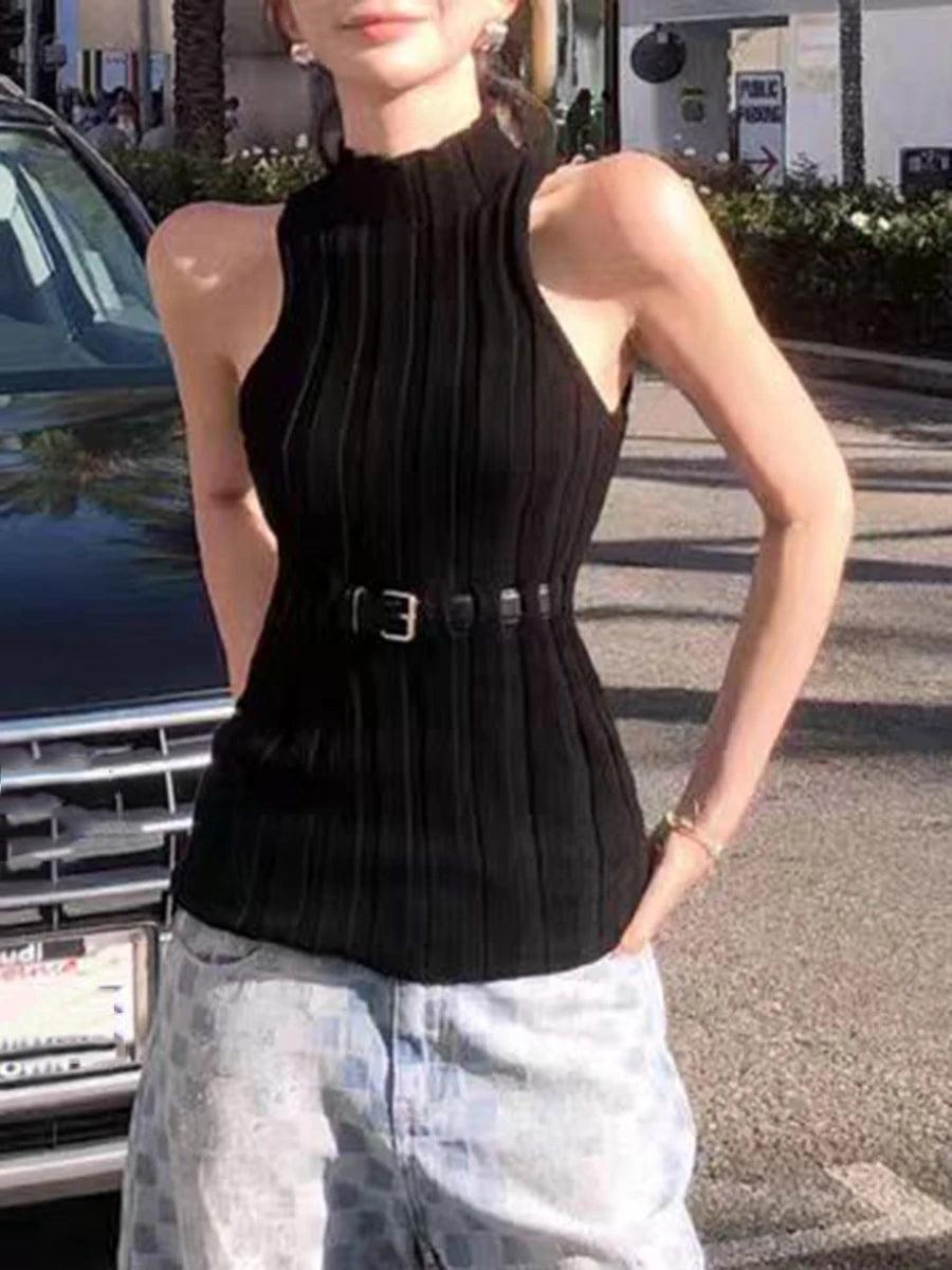 Person wearing a black sleeveless top with a belt and light-colored pants outdoors.