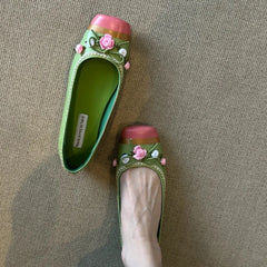 Top-down view of green square toe flats with floral embellishments on a neutral background.