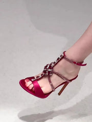 Close-up of a stiletto sandal with red silk upper and crystal embellishments.