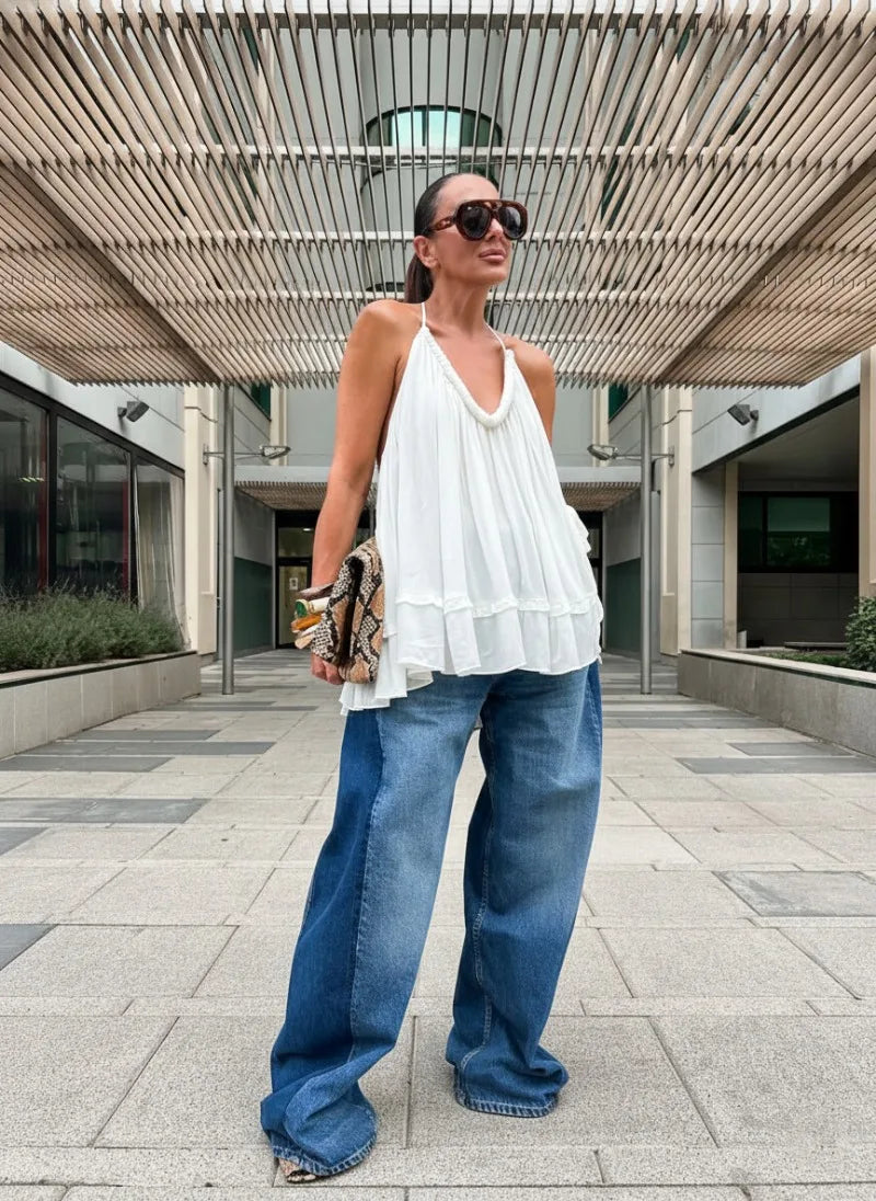 Woman wearing a white top and blue jeans standing outdoors under a modern architectural structure.