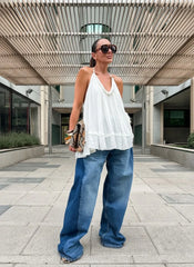 Woman wearing a white top and blue jeans standing outdoors under a modern architectural structure.