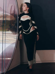 Woman in a black and white outfit standing next to a large circular mirror.