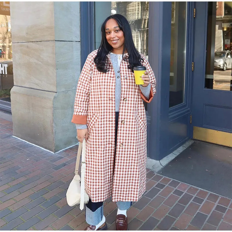 Woman in a checkered coat holding a coffee cup on a city street.