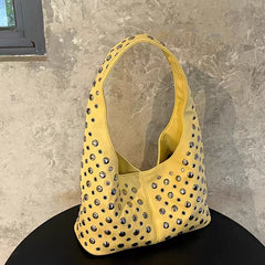Yellow handbag with studded details on a black surface against a stone wall background