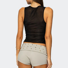 Person wearing a black sleeveless top and gray shorts with embellishments on a white background
