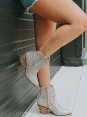 Silver glittery ankle boots with wooden soles worn by a person against a gray wall.