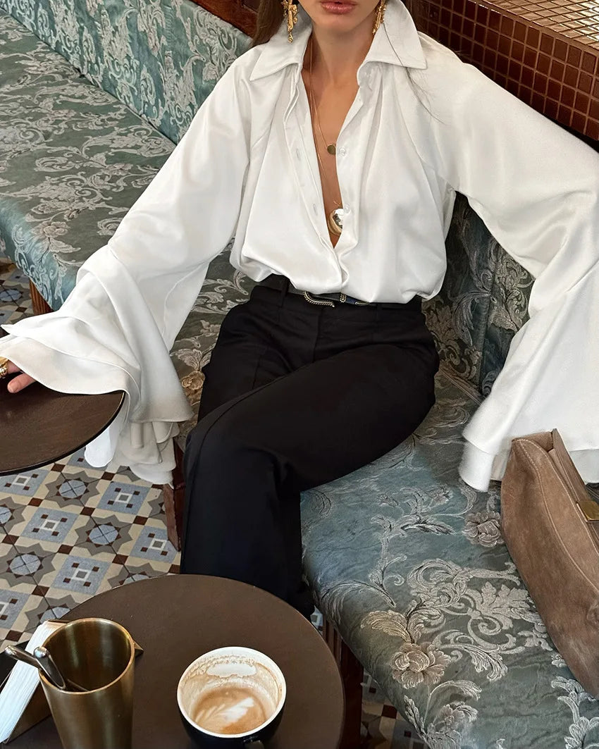 Person wearing a white blouse and black pants sitting in a cafe.