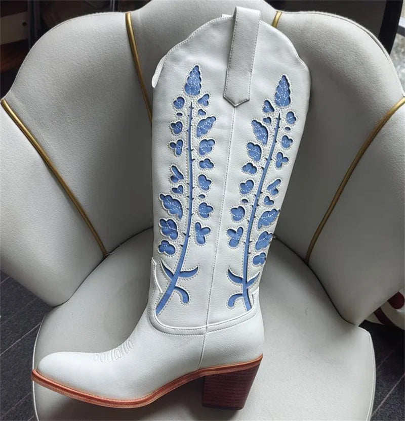 White cowboy boot with blue floral embroidery on a white cushion.