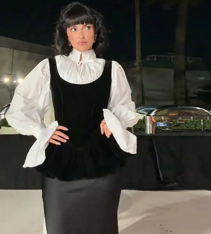 Woman in a black and white outfit standing in front of a table with food at night.