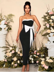 Woman in a black and white strapless dress standing in front of floral decorations.