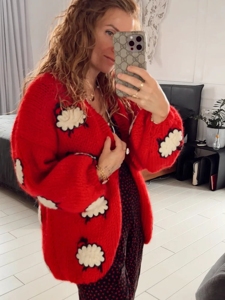 Person wearing a red cardigan with white floral patterns, taking a mirror selfie.