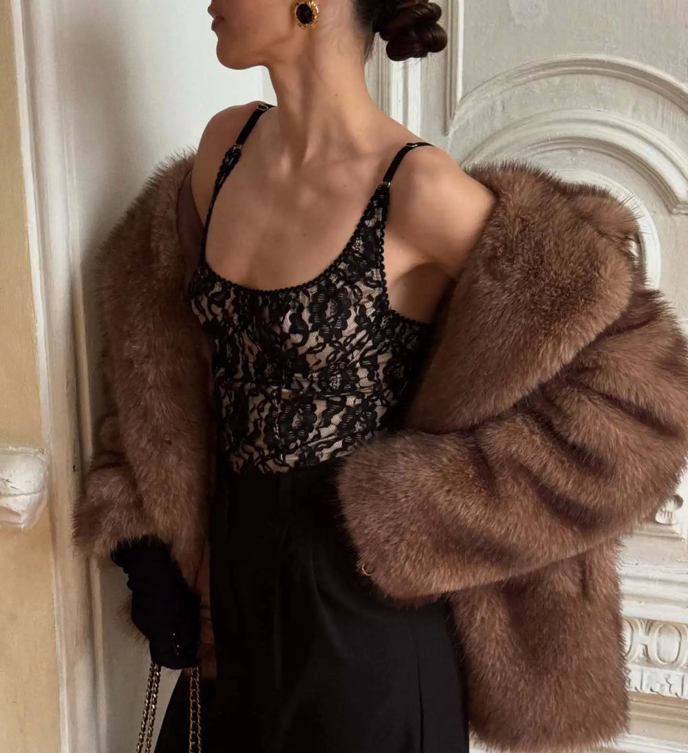 Person wearing a brown fur coat over a black and gold patterned top, standing indoors.