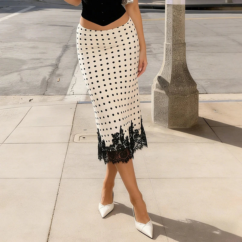 Person wearing a white skirt with black polka dots and lace trim on a sidewalk.