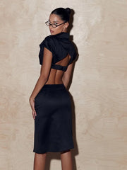 Woman wearing a black outfit with open back against a beige wall