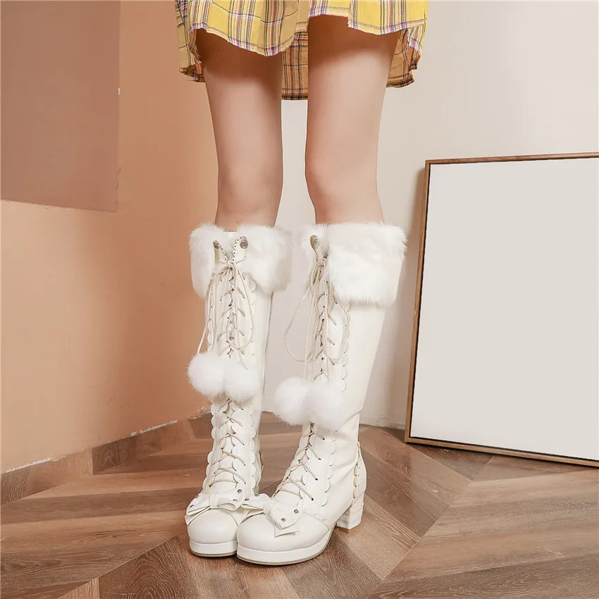 White knee-high boots with fluffy white pom-poms worn by a person in a plaid skirt.