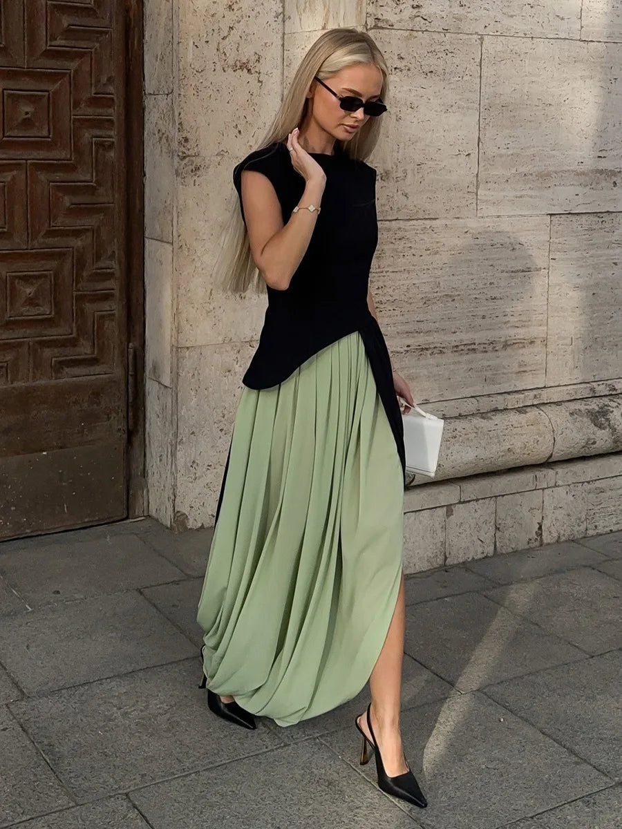 Woman wearing a black top and green skirt standing against a stone wall.