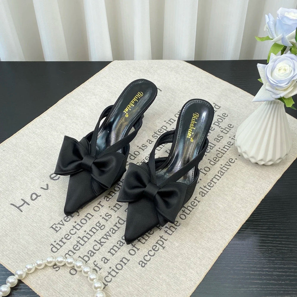 Black high-heeled shoes with bow details on a textured surface.