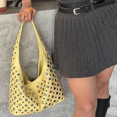 Person holding a yellow handbag with cut-out design, wearing a gray skirt and black boots.
