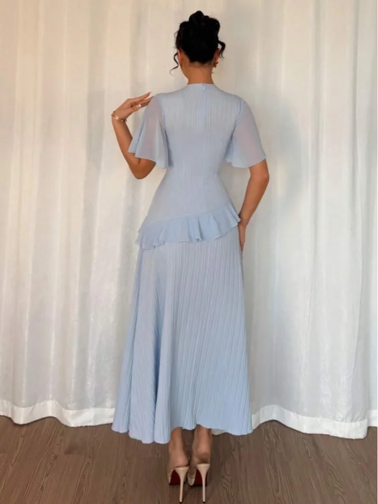 Woman wearing a light blue dress standing against a white curtain.