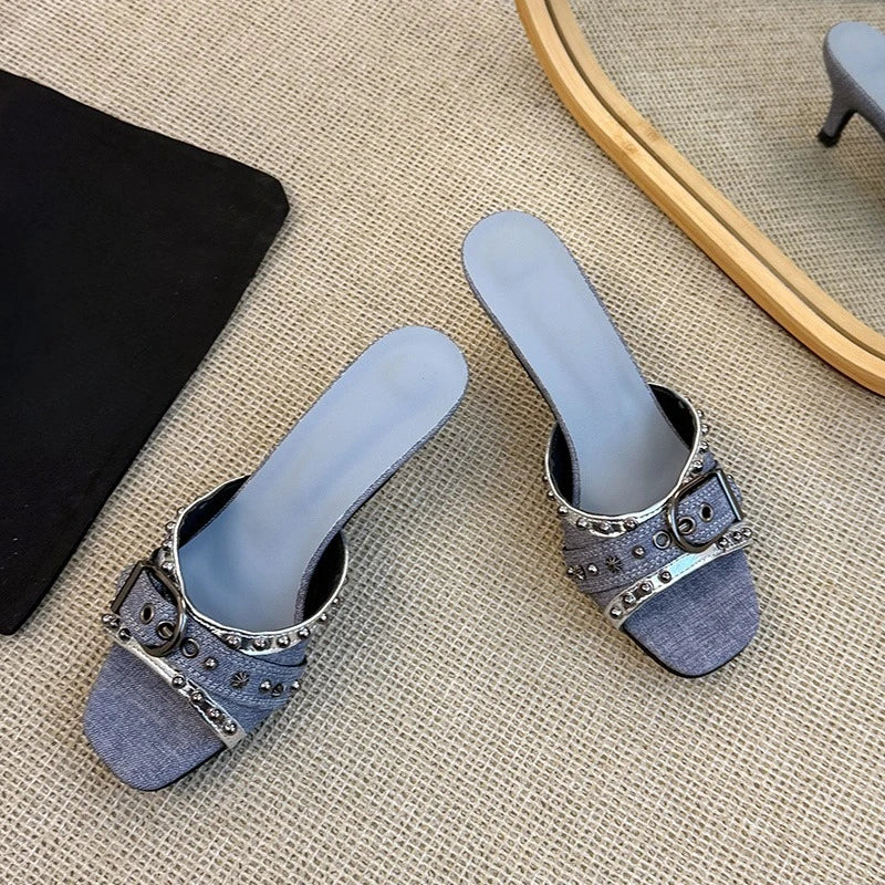 Close-up of black denim kitten heel with decorative metal buckle.