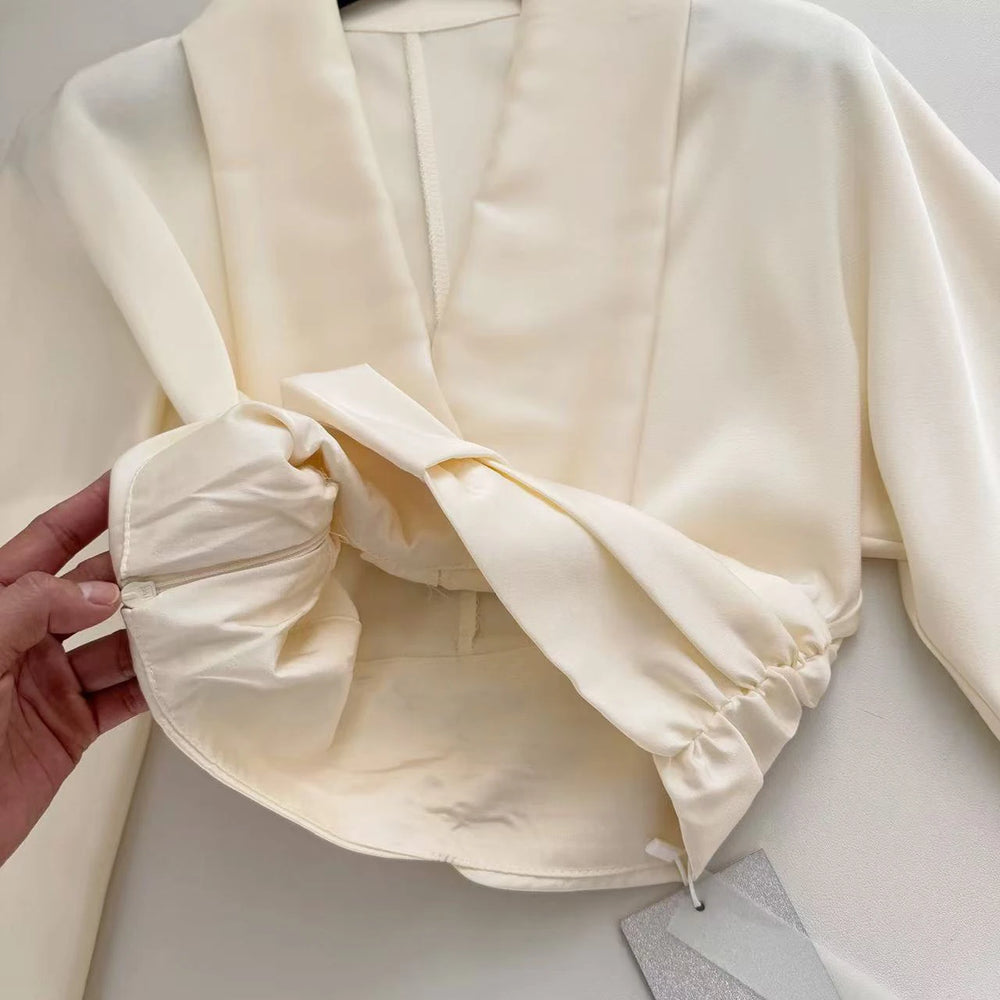 Close-up of a cream-colored garment with a hand adjusting the fabric.