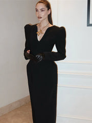 Woman wearing a black dress with long sleeves and gloves in an indoor setting.